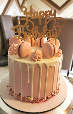 a birthday cake is decorated with pink icing and gold lettering that says happy birthday