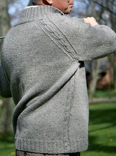 an older man in a gray sweater is holding his hands behind his back as he stands on the grass