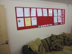 a red bulletin board mounted to the side of a white wall next to a couch