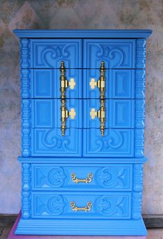 a blue painted dresser with gold handles and knobs on the doors is shown in front of a wall