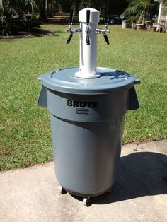 a grey trash can sitting on top of a sidewalk next to a grass covered field