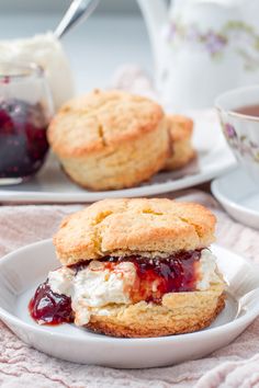 two scones filled with ice cream and jelly on a plate next to a cup of tea