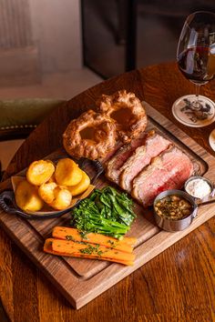 a wooden cutting board topped with meat and veggies next to a glass of wine