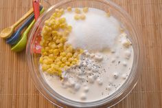 a bowl filled with corn next to two spoons on top of a wooden table