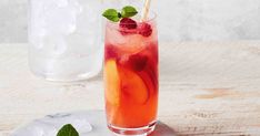 a tall glass filled with ice, fruit and mint garnish on a white plate