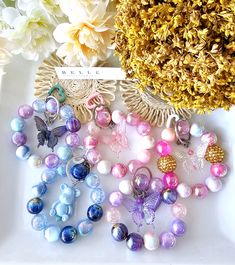 several different colored beads on a white plate next to some flowers and a gold brooch