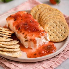 a white plate topped with crackers and salmon covered in marinara sauce next to crackers