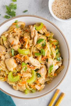 a white bowl filled with chicken and vegetables next to chopsticks on a table