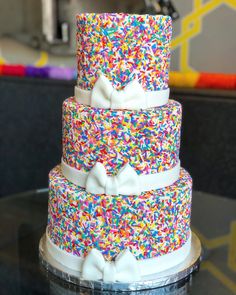 a multi - layer cake with sprinkles and bows on top sits on a table