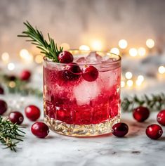 a cranberry cocktail with rosemary garnish in a glass surrounded by christmas lights