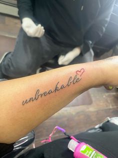 a person with a tattoo on their arm that says unbreakable in cursive writing