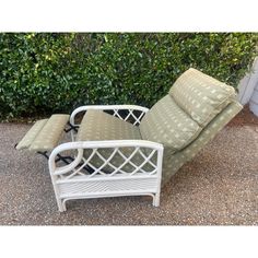 a white reclining chair and ottoman in front of a bush