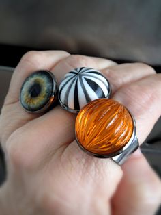 "Retro and so much fun -- bright, neon orange pumpkin ring for Halloween! This fluorescent orange ribbed acrylic vintage cabochon has incredible visual depth -- it reflects light as if it were glowing! The vintage cabochon is set in a black bezel on a flexible metal, decorative gothic filigree adjustable ring band. The ring fits most adults (size 5 to 9), but it may be loose on smaller fingers. - Vintage acrylic orange cabochon: 3/4\" (18mm) dia, 1/2\" (12mm) tall - Flexible black filigree ring: Vintage Black Rings For Halloween, Fun Orange Jewelry For Halloween, Fun Orange Halloween Jewelry, Ring Trick, Gothic Filigree, Black Band Ring, Pumpkin Ring, Halloween Ring, Goth Halloween