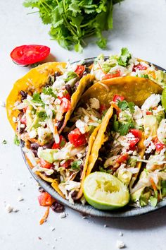 two tacos are on a plate with limes and cilantro