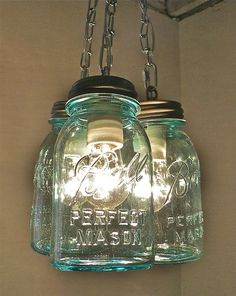 two mason jars are hanging from a chain on the wall, one has a light bulb in it