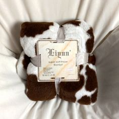 a brown and white cow print blanket on top of a bed next to a tag