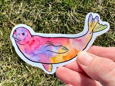 a hand holding a watercolor sticker with a seal on it's side