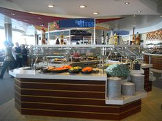 a buffet area with food on the counter and people walking around in the room behind it