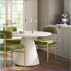 a white table with green chairs around it in a room that has beige walls and wood flooring