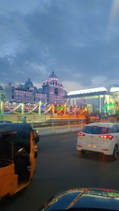 cars driving down the road in front of a building with lights and decorations on it