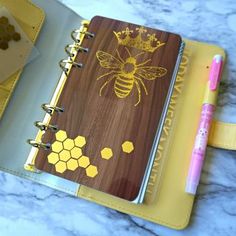 a wooden notebook with honeycombs and a bee on it next to a pen