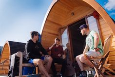 three men sitting in chairs on the deck of a small wooden boat, talking to each other