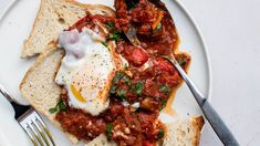 a plate with bread, eggs and tomato sauce on it next to a knife and fork