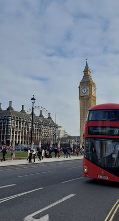 a red double decker bus driving down a street next to tall buildings and a clock tower