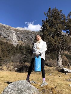 a woman standing on top of a mountain holding a blue bag