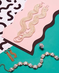 some jewelry is laying on top of a table next to a pink and green background