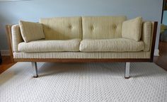 a beige couch sitting on top of a white rug next to a wooden frame chair