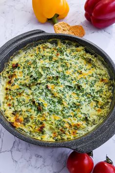 a casserole with spinach and cheese in a pan next to some tomatoes