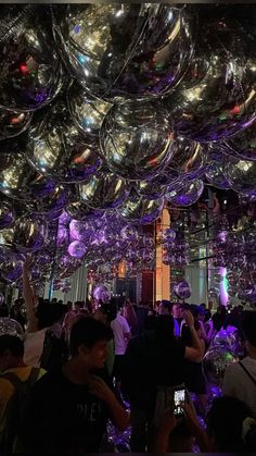 many people are standing around in a room full of shiny glass balls hanging from the ceiling