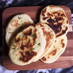 four flat breads on a wooden cutting board with parsley sprinkled on top