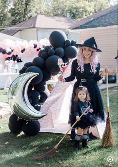 a woman and child dressed up in halloween costumes with black balloons, witch hats and brooms