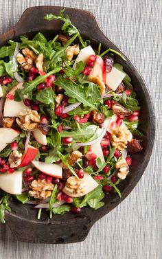 a salad with apples, walnuts and spinach in a bowl on a table