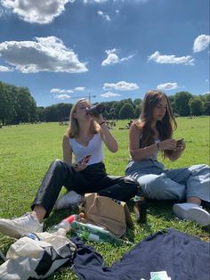 two women sitting on the grass drinking from bottles