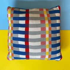 a multicolored pillow sitting on top of a yellow and blue table next to a wall