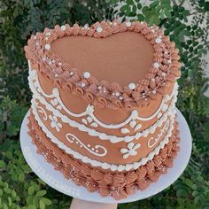 a heart shaped cake sitting on top of a white plate in front of some bushes