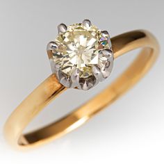 a yellow gold engagement ring with a round diamond center stone, set on a plain white background