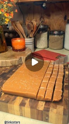 a wooden cutting board topped with cheese on top of a counter next to jars and utensils