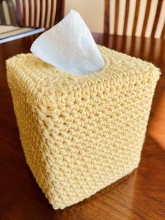 a crocheted tissue box sitting on top of a wooden table next to a chair