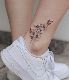 a woman's foot with a flower tattoo on her left ankle and white sneakers