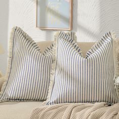 two blue and white striped pillows sitting on top of a couch next to a painting