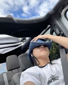 a woman sitting in the driver's seat of a car wearing a blue hat