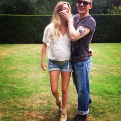 a man standing next to a woman on top of a lush green field with trees in the background