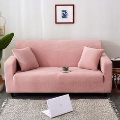 a pink couch sitting on top of a rug next to a laptop computer and potted plant