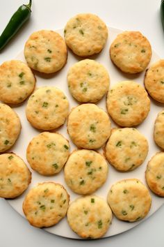 small crackers are arranged on a white plate with green chili peppers in the background