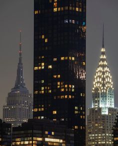 the empire building is lit up at night in new york city, with other skyscrapers behind it