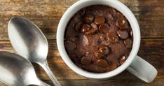 a bowl of chocolate pudding with two spoons next to it on a wooden table